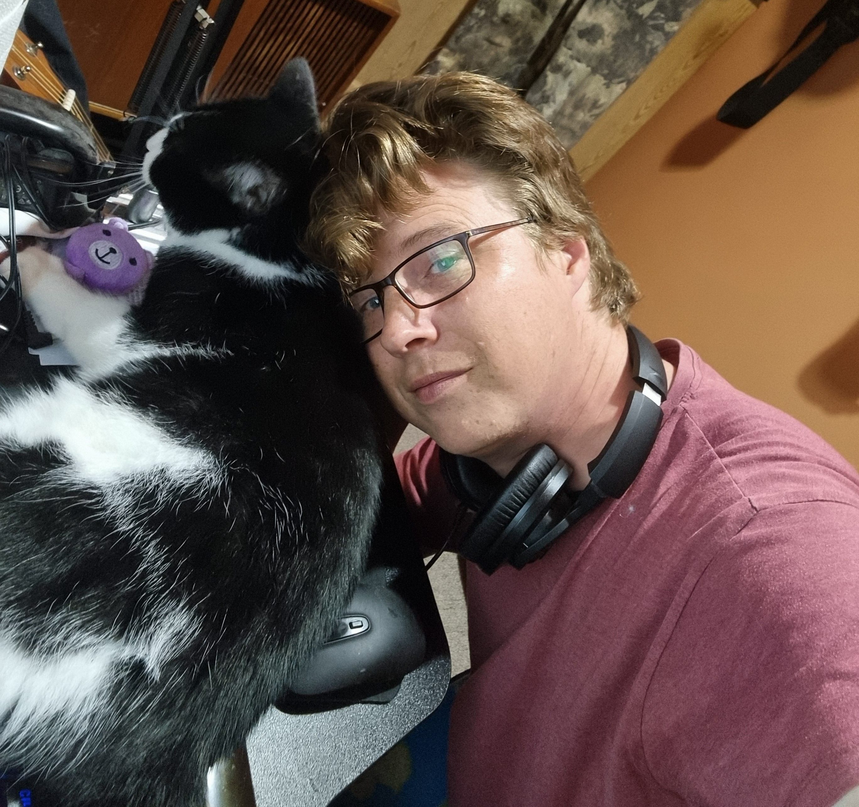 Man leaning over a black and white cat that is laying on the desk in a home studio